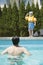 Portrait of son with snorkeling equipment standing by the pool as father waits in the water