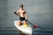 Portrait of a sporty handsome man in sunglasses sitting on a rowing board with an oar in his hands and posing for the camera.