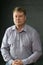 Portrait of a strict blonde adult man on a gray background 40-45 years old in a blue shirt