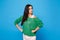 Portrait of strict young woman in green casual clothes looking camera, stand with arms akimbo on waist isolated on