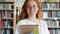 Portrait of student pretty girl holding books in university library smiling