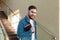 Portrait of student on stairs. Caucasian smiling handsome bearded man with backpack notebooks in university campus steps.