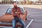 Portrait of a stylish bearded male in old-fashioned clothes sits on the hood retro car in the city parking.