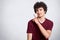 Portrait of stylish handsome young teenager isolated on white background. Dark haired curly student smiles and points aside.