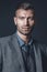 Portrait of stylish successful brutal man in gray suit with fashionable haircut on background of gray wall