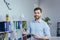 Portrait of a successful business founder, a man looks at the camera and smiles at a white board for notes, holding a tablet,