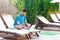 Portrait of successful handsome bearded young adult writer man in blue tshirt and shorts sitting on cozy sunbed with laptop on