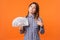 Portrait of successful proud brunette woman wearing checkered shirt holding money. indoor studio shot isolated on orange