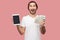 Portrait of suprised handsome bearded young hipster man in white shirt and casual hat standing, holding empty screen ipad and