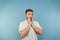 Portrait of a surprised adult man in a white T-shirt stands on a blue background and holds his face in shock