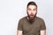 Portrait of surprised bearded man with dark green t shirt against light gray background.