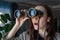 Portrait of a surprised brunette with binoculars looking out the window, spying on neighbors