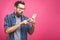 Portrait of a surprised casual man looking at mobile phone isolated over pink background