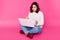 Portrait of surprised casual woman sits on floor with laptop, keeps legs crossed, dressed jeans, sweater and boots. Cute student