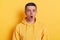 Portrait of surprised man with dark hair wearing casual style hoodie standing isolated over yellow background, sees something