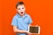 Portrait of surprised schoolboy with tablet and blue t-shirt on orange studio background