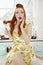 Portrait of a surprised young woman with hair tangled in whisk sitting on kitchen counter