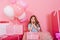 Portrait sweet surprised birthday kid looking to camera suround a lot of giftboxes, balloons  on pink background