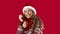 Portrait of sweet young lady wearing woolen sweater, Santa hat and scarf on red background