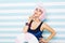 Portrait sylish summer attractive model in blue swimsuit with cut pink hairstyle with big lollipop on striped blue white