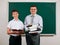 Portrait of a teacher dressed in business suit with folders, documents, posing with schoolboy at blackboard background - learning