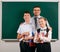 Portrait of a teacher, schoolboy and schoolgirl posing with exercise books, pens, pencils and other school supplies on blackboard