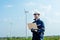 Portrait of technician worker hold laptop and look to left side in front of windmill or wind turbine with blue skay in area of