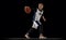 Portrait of teen girl, basketball player in motion, dribbling ball isolated over black studio background