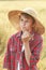 Portrait of teenage farm boy in wide-brimmed hat chewing oat cereal ears straw