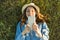 Portrait of teenage girl 14 years old lying on the grass. Girl in dress hat, in her headphones holds a smartphone, listens to musi