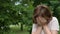 Portrait of a teenage girl standing on the street in a park on a Summer day, covering her face with her hands, crying. A sad child