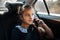 Portrait of teenage girl talking at the smartphone in the backseat of the car.