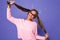 Portrait of teenage woman in sweatshirt wearing trendy sunglasses having fun and touching her ponytails, isolated over violet