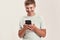 Portrait of teenaged disabled boy with Down syndrome smiling at camera while using smartphone, standing isolated over