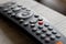 A portrait of a television infrared remote control lying on a wooden table. The focus is on the play and pause button. It can also