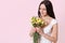 Portrait of tender attractive young woman with long black hair in summer white dress holding bouquet, smelling flowers, isolated