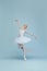 Portrait of tender young ballerina dancing, performing, posing in movement isolated over blue studio background