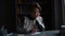 Portrait of thinking pupil boy writing to workbook with pen sitting at desk in dark children room.