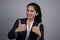 Portrait of a thirty beautiful young business lady in a business suit, showing thumbs up, class, yes, smiling. On a gray
