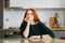 Portrait of thoughtful young woman writing handwritten letter sitting at table with envelope in kitchen room with modern