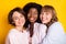 Portrait of three attractive dreamy affectionate cheerful girls bonding embracing isolated over bright yellow color