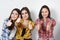 Portrait of three beautiful young happy females smiling joyfully showing thumbs up isolated on white