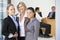 Portrait Of Three Female Executives With Office Meeting In Background