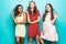 Portrait of Three mixed race best friends posing in studio, wearing summer style dresses against blue wall . Girls smiling and