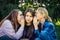 Portrait of three young girlfriends who whisper in the park. Exchange of news, emotional women whispering gossip