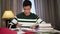 Portrait of tired Asian male college student sitting with books at home. Young handsome boy putting head on hand and