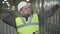 Portrait of tired Caucasian man in helmet and vest yawning and stretching at the background of steel metal pipes