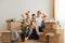 Portrait of tired couple sitting on sofa with children after moving, keeping hands on heads, exhausted of unpacking packages,