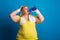 Portrait of a tired overweight woman in studio on a blue background, drinking water.