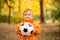 Portrait of toddler boy with soccer ball in autumn park. Healthy childhood, sports and outdoor activities concept